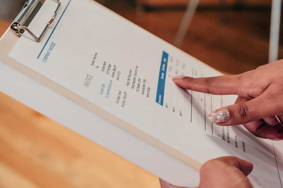 person pointing at invoice on clipboard